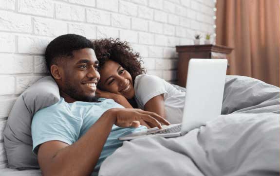 Man and woman smiling at laptop while laying in bed