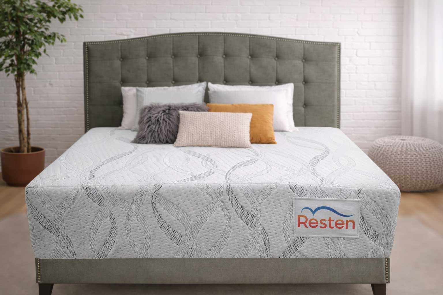 Resten mattress with decorative pillows and a grey headboard in a clean bedroom with white brick wall and wood floors