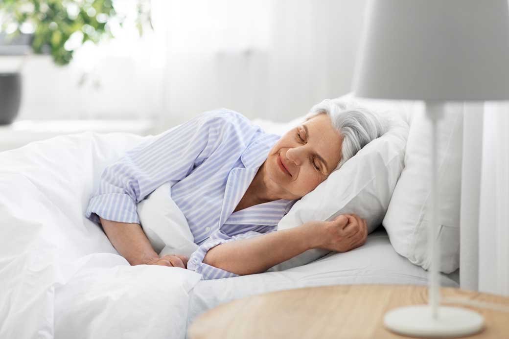 Senior woman comfortably laying in bed with eyes closed in a clean and bright bedroom